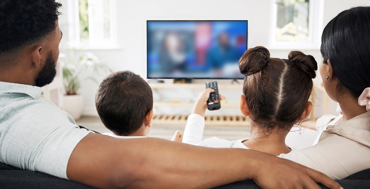 Family watching TV programming from their living room couch, viewed from behind